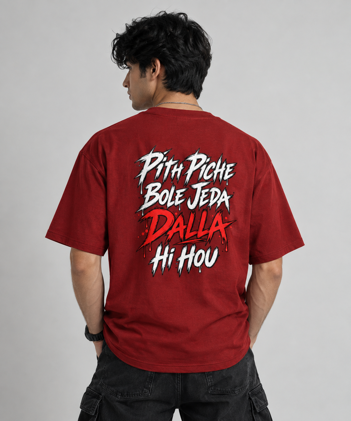 A man wearing a red graphic t-shirt, viewed from behind. The shirt features a bold white and red text design on the back reading 'Pith Piche Bole Jeda DALLA Hi Hou'.