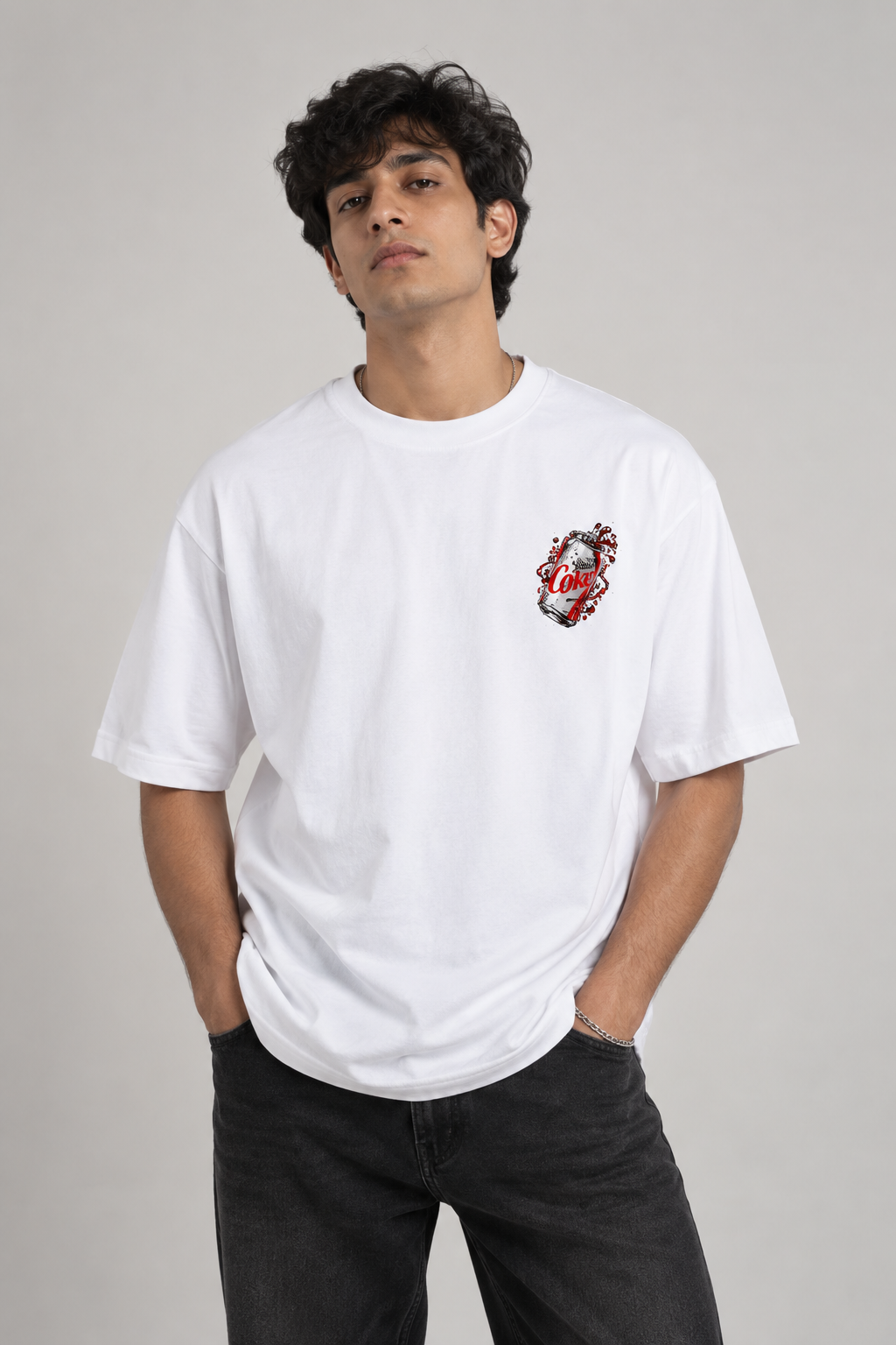 A man wearing a white crewneck t-shirt with a small red and black graphic on the left chest, paired with dark gray jeans, against a plain light gray background.