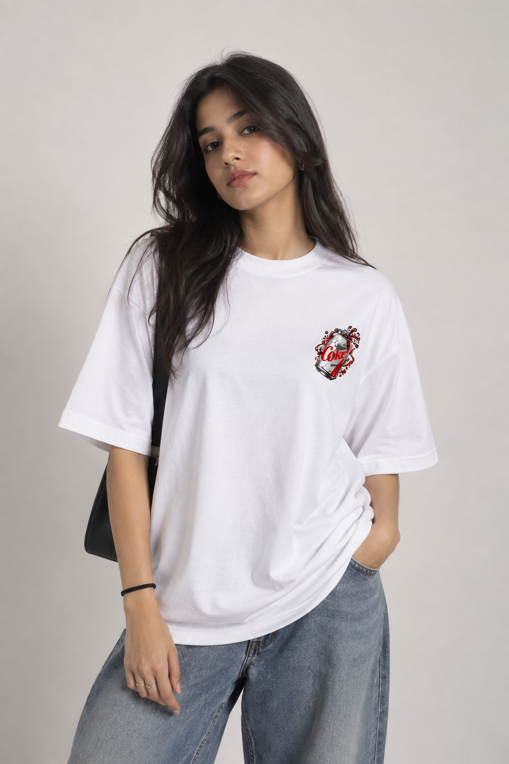 A woman wearing a white oversized short-sleeve t-shirt with a small red and black graphic on the left chest, paired with light blue jeans, against a plain light gray background.