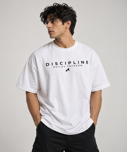 A man wearing a white short-sleeve t-shirt with a black graphic print that reads 'DISCIPLINE BUILDS FREEDOM' and a small silhouette of a person jumping, paired with black cargo pants, against a light gray studio background.