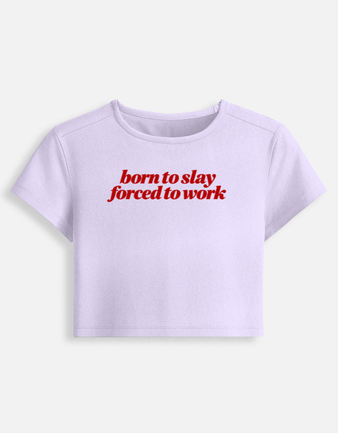 A light lavender short-sleeve crop top t-shirt with the phrase 'born to slay forced to work' printed in red across the chest, displayed on a clean off-white background.