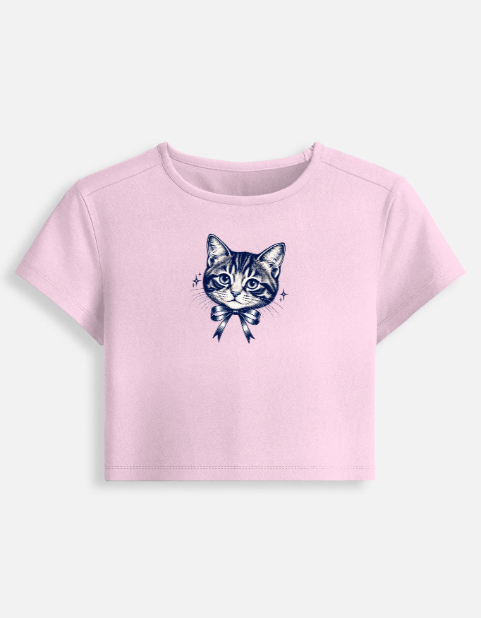 A light pink short-sleeve crop top featuring a detailed navy blue graphic of a tabby cat wearing a bow on the front, displayed against a light gray background.