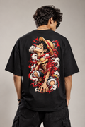 A man wearing a black graphic t-shirt, viewed from behind. The shirt features a large, detailed back print of the anime character Luffy from One Piece, depicted with his straw hat and surrounded by red and white waves.