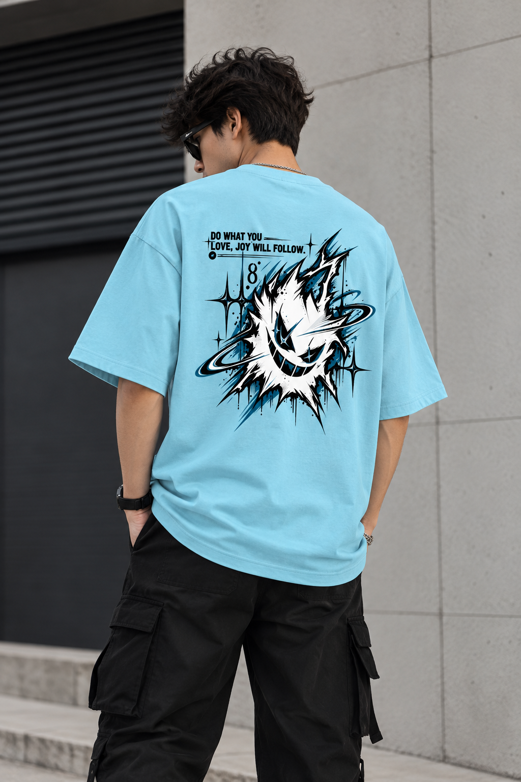 A man wearing a light blue oversized graphic t-shirt, viewed from behind. The shirt features a large black and white circular explosion-style graphic with the text 'DO WHAT YOU LOVE, JOY WILL FOLLOW' and the number 18.