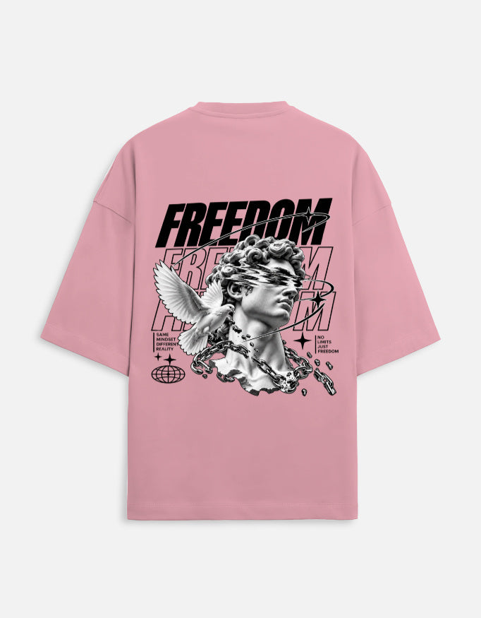 A pink oversized short-sleeve t-shirt shown from the back, featuring a large black and white graphic print of a classical statue head with a winged figure, the word 'FREEDOM' in bold black letters, and smaller text details.