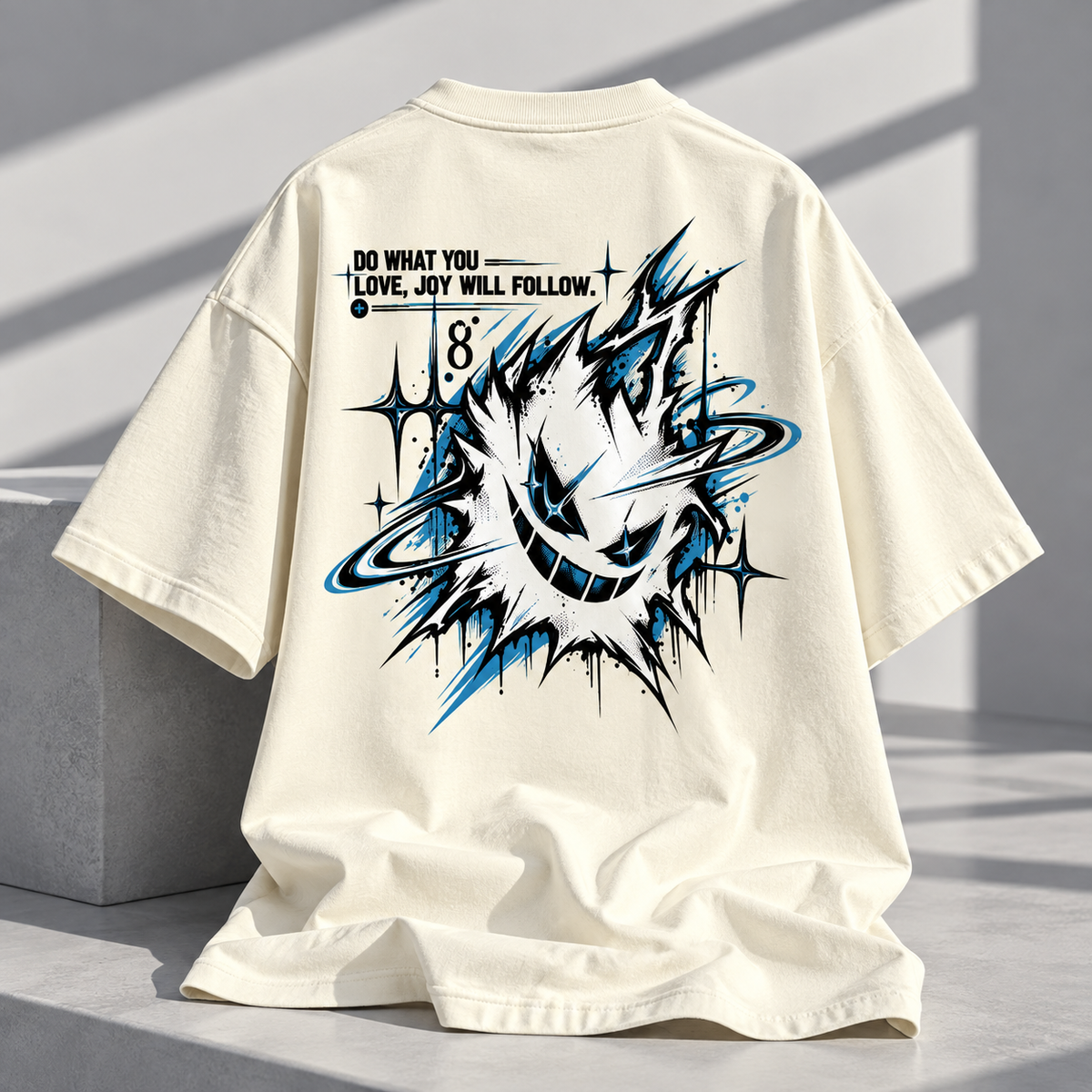 An oversized cream-colored t-shirt displayed on a concrete ledge, showing the back graphic. The design features a stylized blue and black cartoon character with a ring around its head, accompanied by the text 'DO WHAT YOU LOVE, JAY WILL FOLLOW.