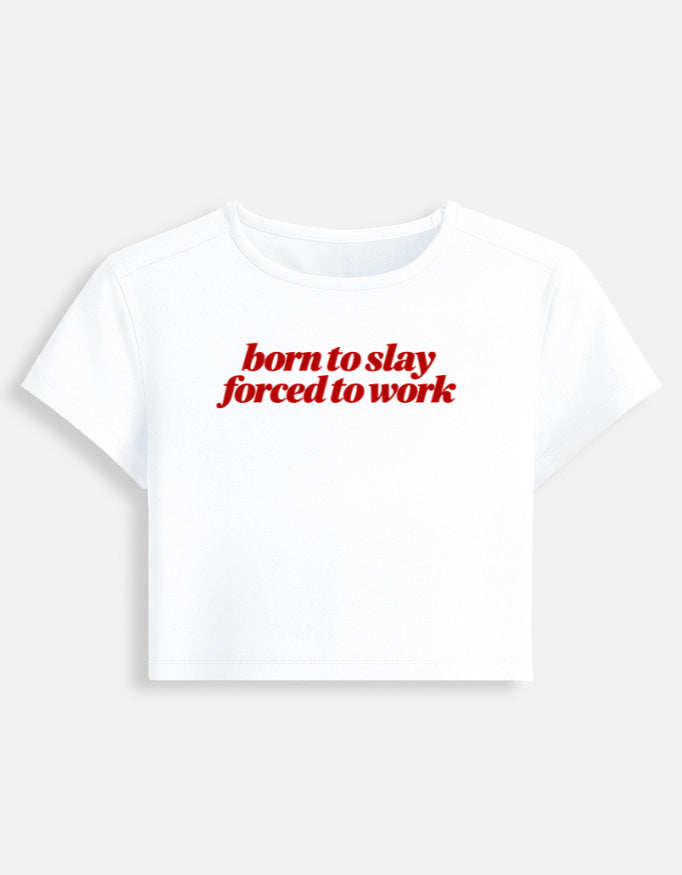 A white short-sleeve crop top t-shirt with the phrase 'born to slay forced to work' printed in red across the chest, displayed on a light gray background.